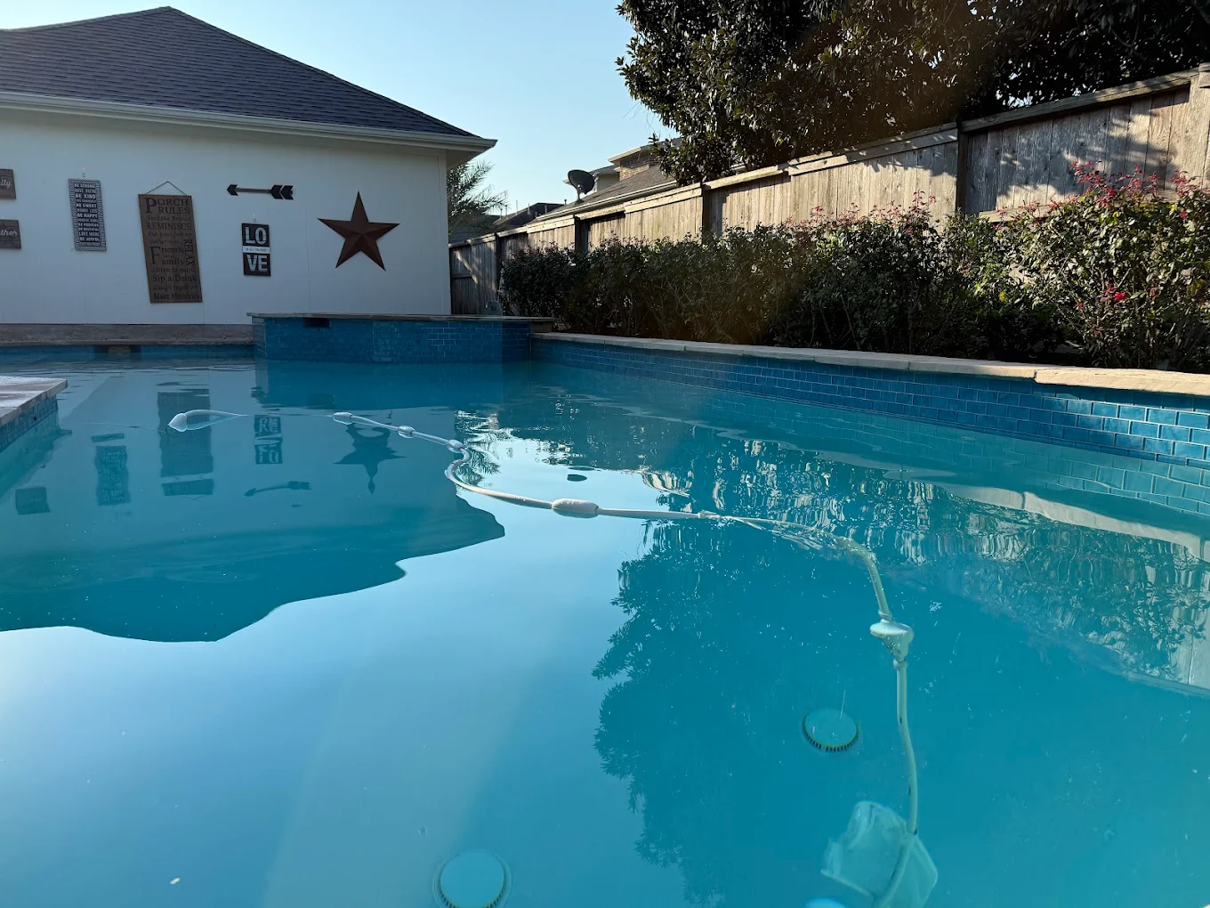 Clear backyard pool with a blue glass tile waterline and an automatic pool cleaner hose