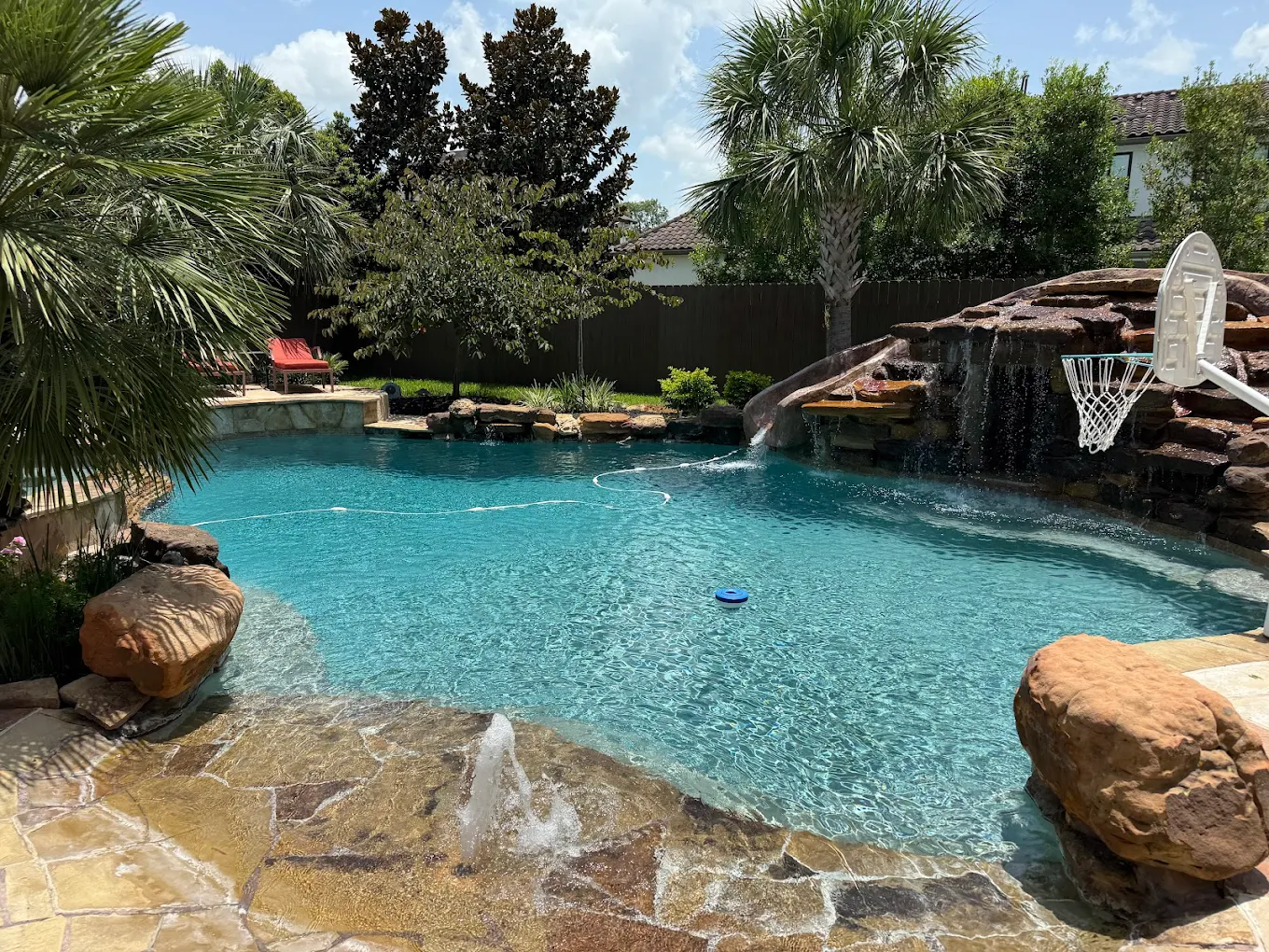 Freeform pool with a rock grotto waterfall, slide, and flagstone beach entry under palm trees