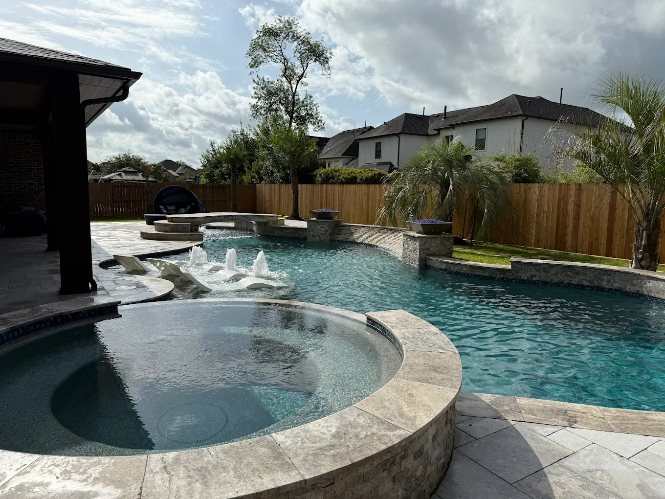 Round raised spa with a stone veneer wall beside a freeform pool with bubblers and fire bowls