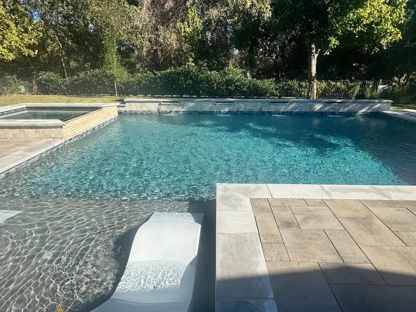 Geometric pool with a raised spa, sheer water features, and a tanning ledge lounger